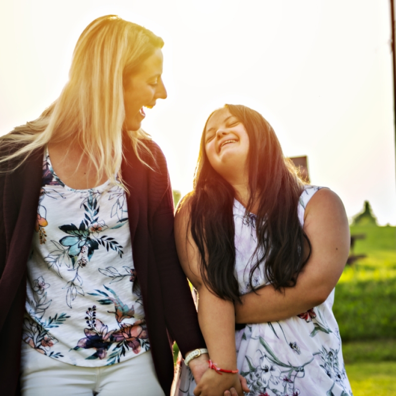 A Portrait of trisomie 21 adult girl smilin outside at sunset with family friend